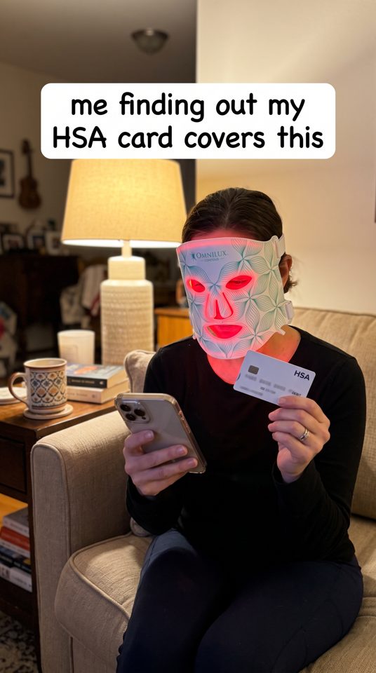 Omnilux spec static: a woman wearing the LED mask holds her HSA card